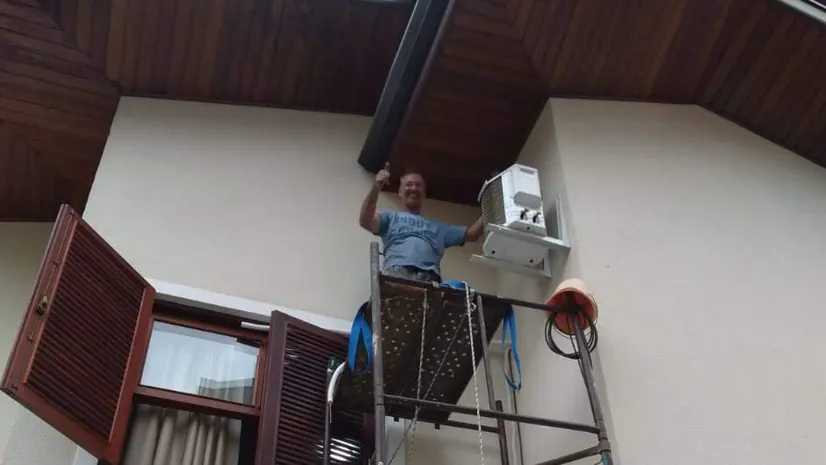 Técnico em andaime instalando ar-condicionado no alto de uma fachada